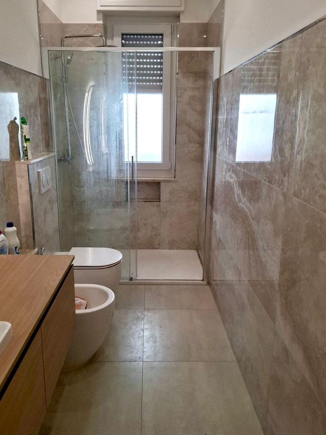 Bagno con grandi lastre effetto travertino e box doccia in cristallo